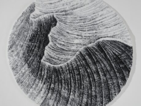 Abyss & Habidecor round gray rug with a swirling, ridged pattern resembling waves in black and white.