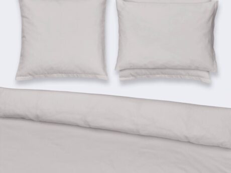 Christian Fischbacher Jersey Uni bed linen set styled on bed with duvet cover and pillowcases in plain light grey stretch cotton jersey, minimal bedroom setting