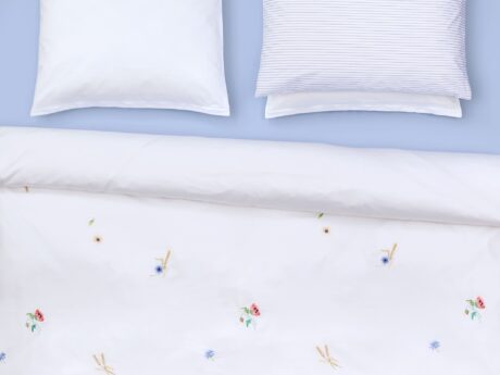 Christian Fischbacher Summerfield bed linen styled on bed with white Pima cotton satin duvet cover featuring scattered wildflower print with poppies and cornflowers on blue background