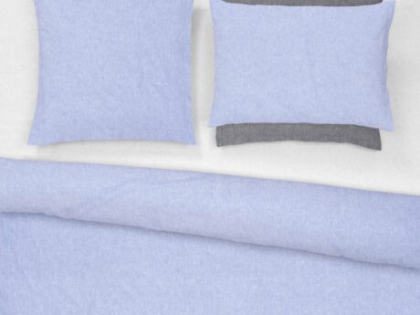 Christian Fischbacher Morning Sky bed linen set styled on bed with duvet cover and pillowcases in soft blue melange flannel with dark grey reverse